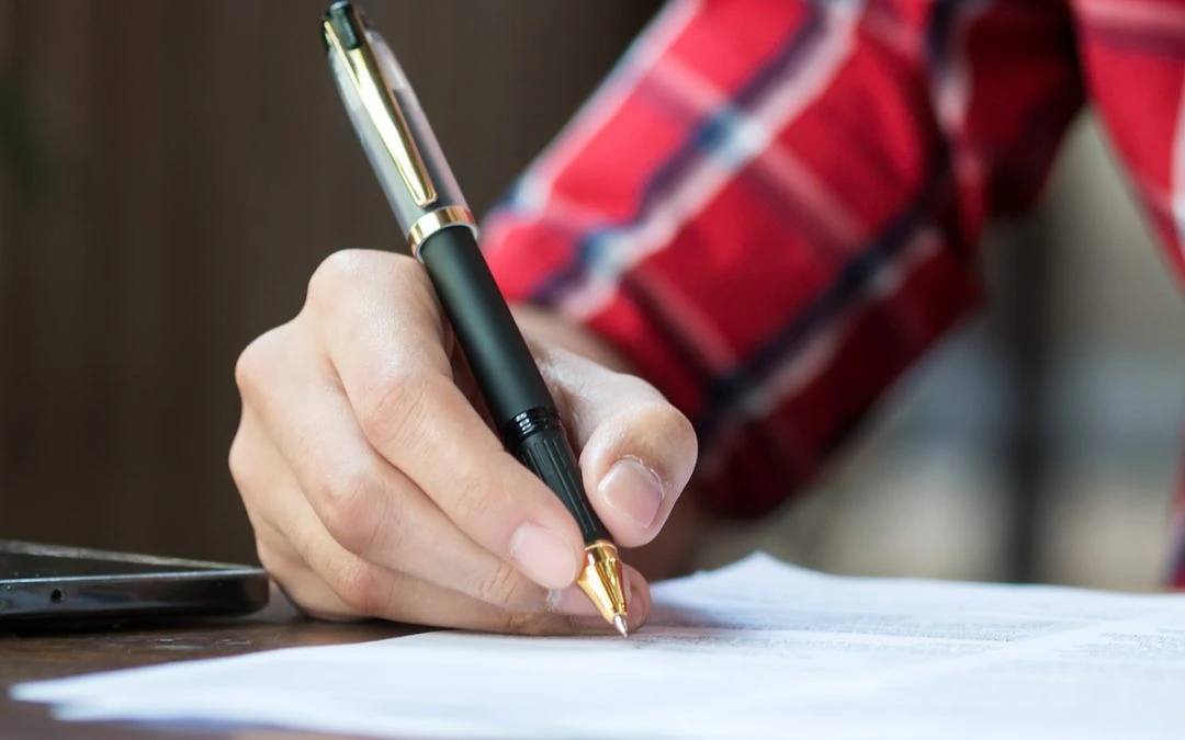 A hand writes a letter with a pen
