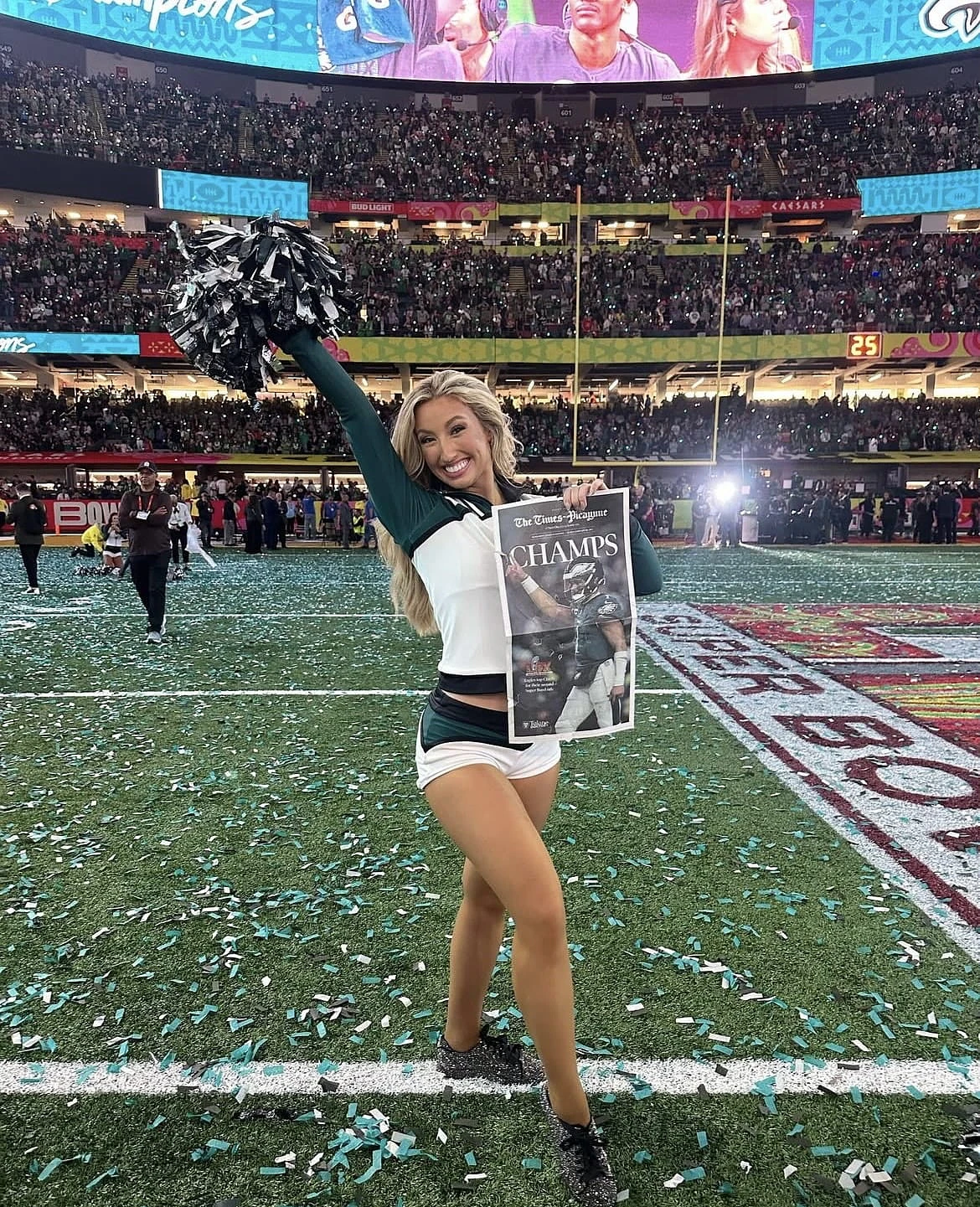A cheerleader celebrates on a confetti-strewn football field, holding a newspaper with the headline "CHAMPS."