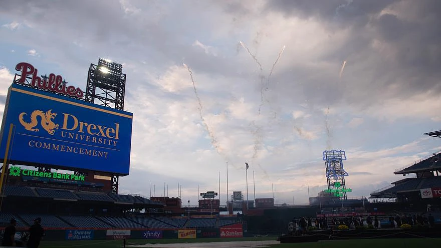 Fireworks light up the sky over Citizens Bank Park during Drexel University’s commencement, with a prominent Phillies sign in the background.