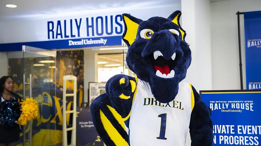 A mascot in a Drexel University jersey poses in front of a store called "Rally House."