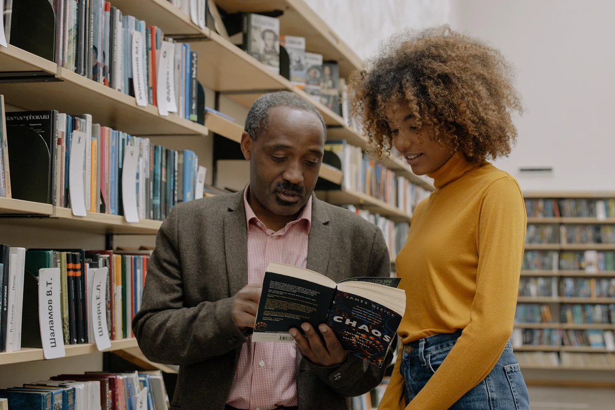 A professor and student look at a book together in the library
