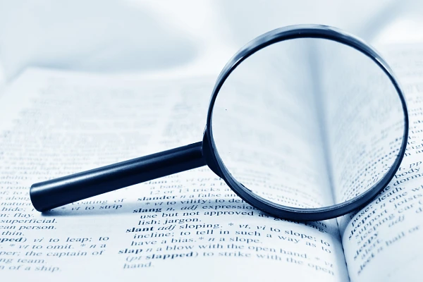 A magnifying glass is placed on an open book, enlarging the text beneath it.