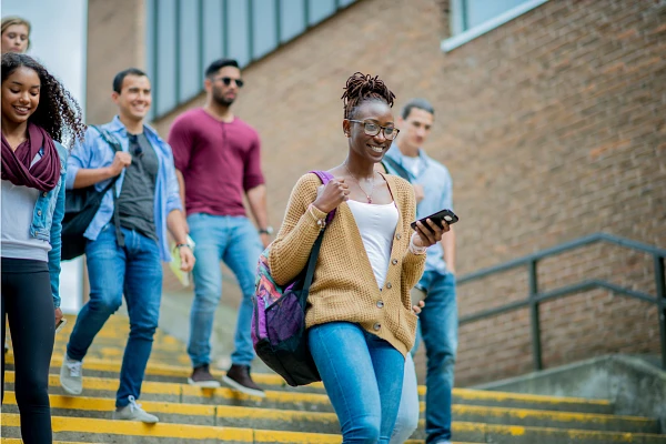 A group of young adults joyfully walking down stairs, with one person focused on their phone.